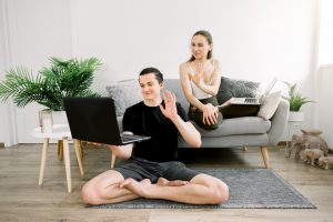 Young joyful couple of yoga coaches, sitting in lotus position, having fun at home after yoga